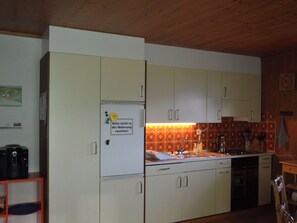Eine Küche mit weißen Schränken, einem Kühlschrank mit einem Zettel, einer Spüle und einer Holzbalkendecke.