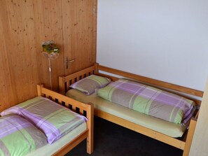 A small room with two wooden bunk beds, a wooden wardrobe, and a small shelf with items. - Wohnung Hof Coms, (Urmein), by Interhome (Urmein)
