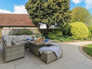 A patio with wicker furniture, a table set with blue plates and bowls, and a large tree in the background. - Sea Estate House (Littlehampton)