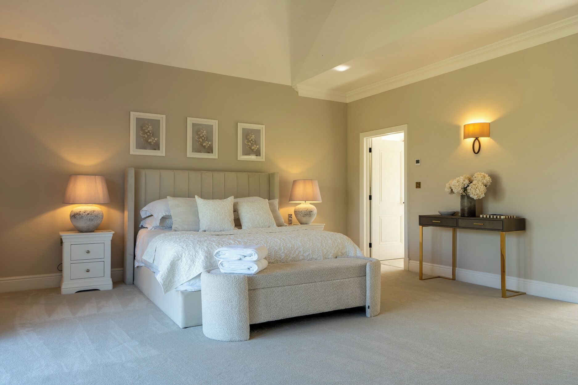 A bedroom with a bed, bedside lamps, a nightstand, a console table, and a door.