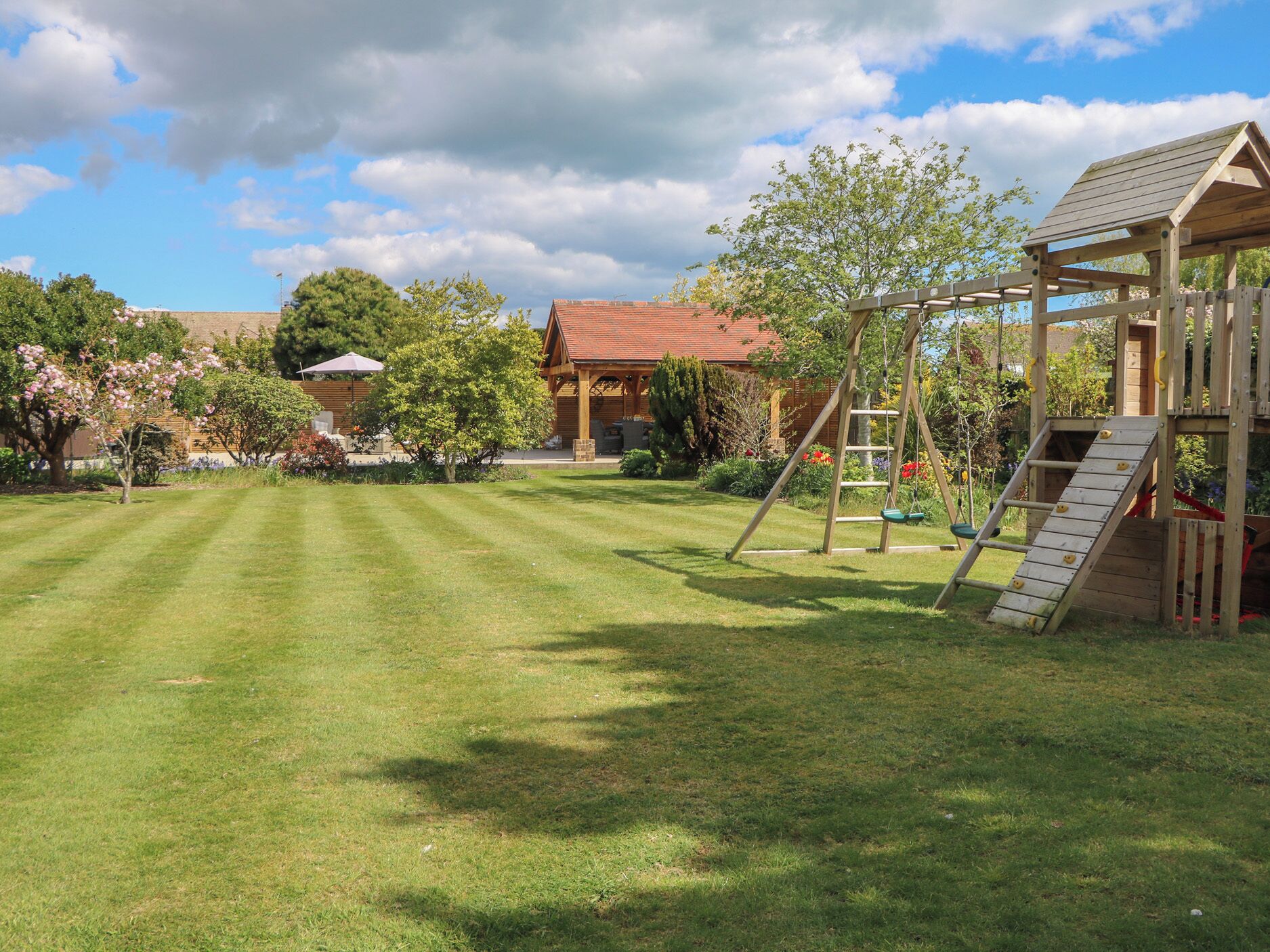 A well-maintained garden with a wooden play structure, a swing set, and a covered seating area.