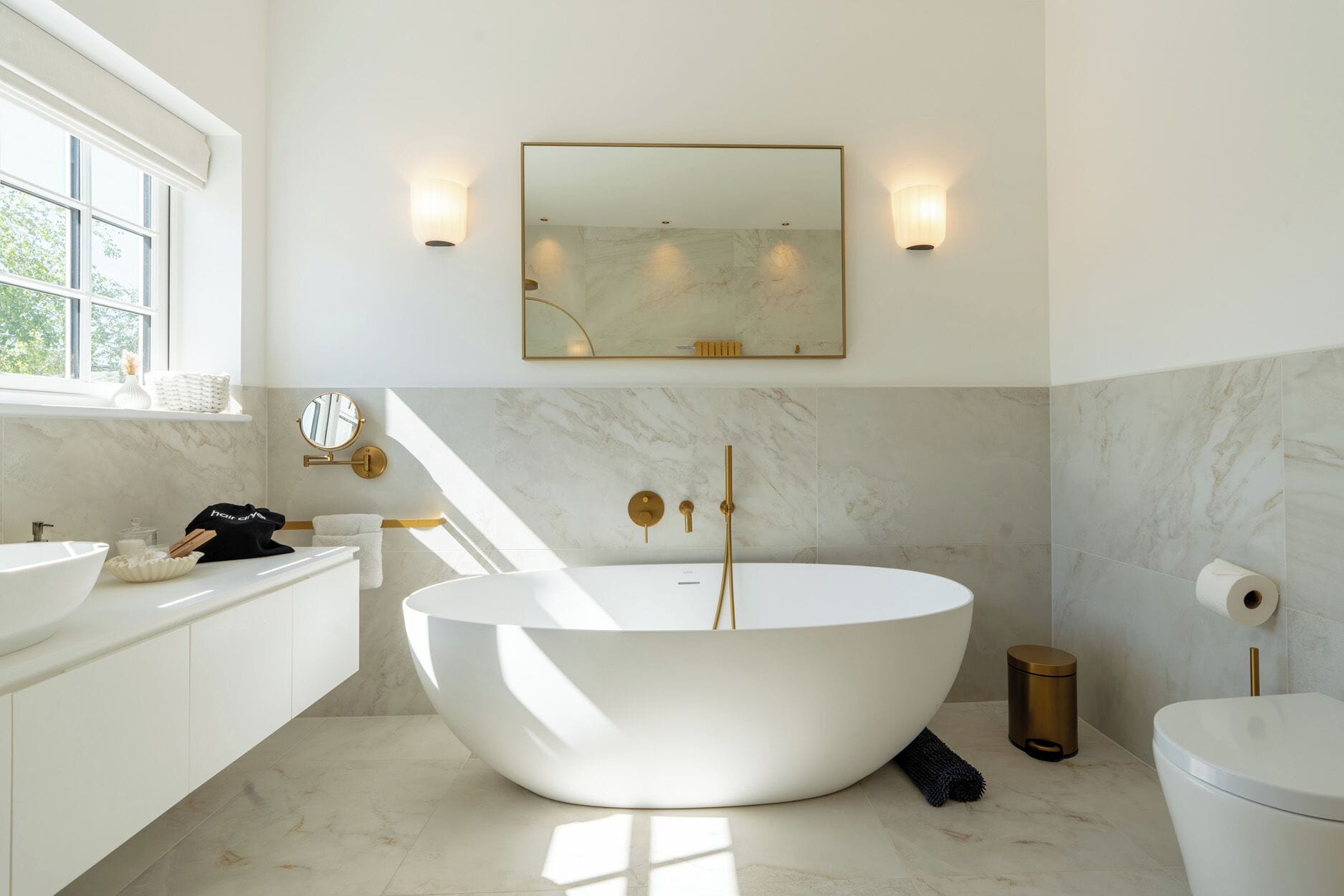 A modern bathroom with a freestanding bathtub, a vanity with a sink, a toilet, and a window providing natural light.