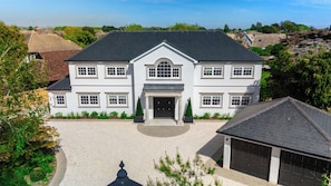 Ein großes, zweistöckiges Haus mit symmetrischer Fassade, einem zentralen Eingang und einer Auffahrt zu einer Garage.