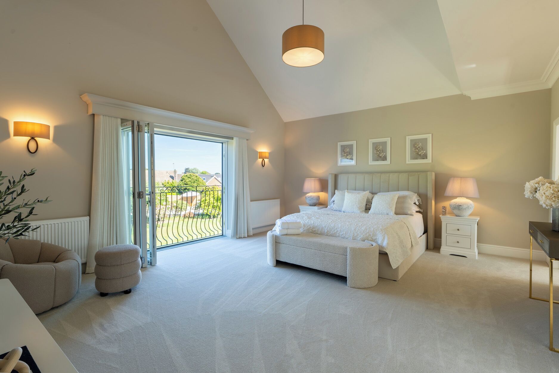 A bedroom with a large bed, a sitting area with a chair, a bedside table with a lamp, and a view through a sliding door to the outside.
