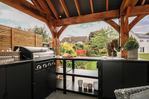 Eine Außenküche mit Grill, Spüle und Blick auf Garten und Häuser.
