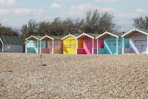 A row of colorful beach huts with a pebbled beach in the foreground.