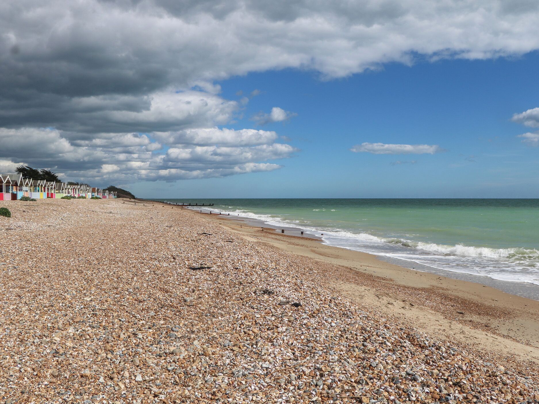 A pebbled beach with colorful beach huts and a clear sky.