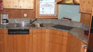 A kitchen with wooden cabinets, a granite countertop, a stainless steel sink, a coffee maker, and a refrigerator.