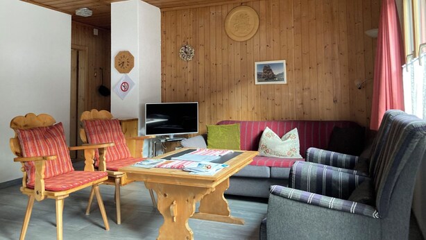 A wooden-paneled room with a sofa, chairs, a table, a TV, and wall decorations.