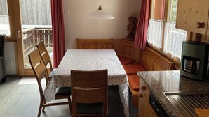 A kitchen with a dining table, chairs, a hanging light, and a stove.