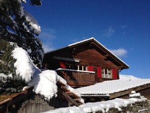 Una cabaña de madera con techo inclinado, rodeada de árboles cubiertos de nieve.