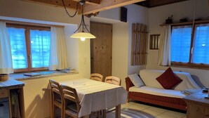 Ein gemütliches Zimmer mit Esstisch, Stühlen, einer Couch und einem Fenster mit Vorhängen.