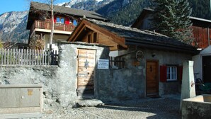 Ein Steinhaus mit einer Holztür, einem Balkon mit roten Geländern und einem Berg im Hintergrund.
