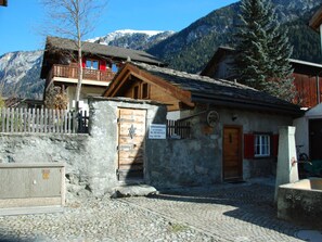 A stone building with a wooden door, a balcony with red railings, and a mountain backdrop.