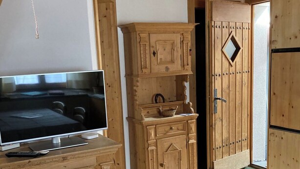 Ein Zimmer mit einem Bett, Holzschränken, einem Fernseher und einer Tür mit einem rautenförmigen Fenster.