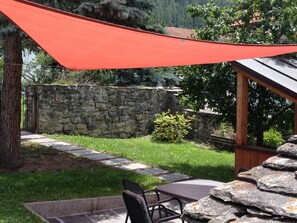 A stone wall, a wooden pergola, and a table with chairs in a garden setting.