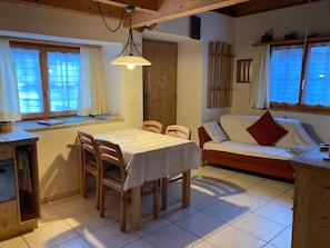 A cozy room with a dining table, chairs, a sofa, and a window with blinds. - Haus Fravgia veglia, (Andeer), by Interhome (Andeer)