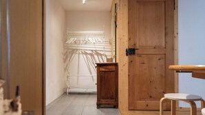 Un couloir avec une porte en bois, une petite armoire en bois et une chaise blanche.