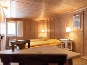 Una stanza con rivestimento in legno, un letto, due comodini con lampade, una sedia e una finestra con tende.