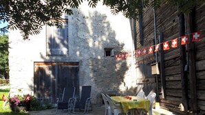 Un bâtiment en pierre avec une porte en bois, une table entourée de chaises et un drapeau suisse en guise de décoration.