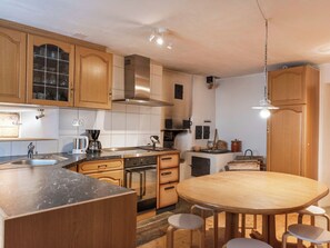 Una cucina moderna con mobili in legno, cappa aspirante in acciaio inossidabile, forno integrato, macchina da caffè e un tavolo rotondo in legno con sgabelli.