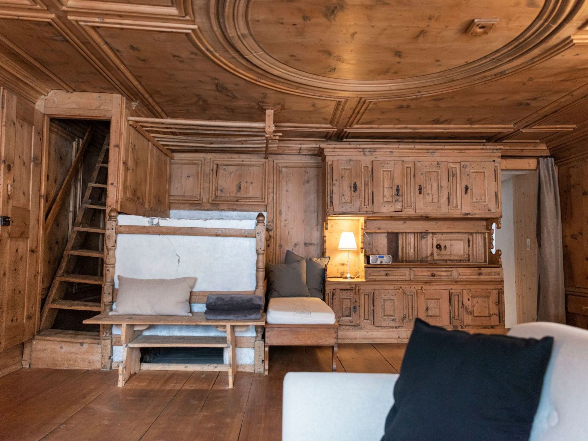 Interior de una cabaña de madera con una litera, un sofá, una radio y una escalera.