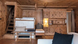 L’intérieur d’une cabane en bois, avec un lit superposé, un bureau, une chaise, une lampe et une radio.