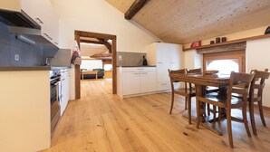 A kitchen with wooden flooring, white cabinets, and a dining area with wooden chairs. - Wohnung von Schorsch, (Splügen), by Interhome (Splügen)