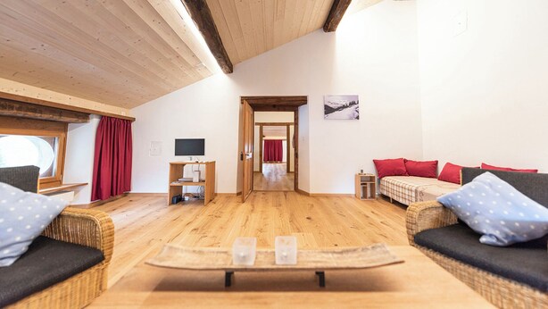 A cozy room with a wooden ceiling, a television, a sofa, a bed, and a small table with glasses. - Wohnung von Schorsch, (Splügen), by Interhome (Splügen)