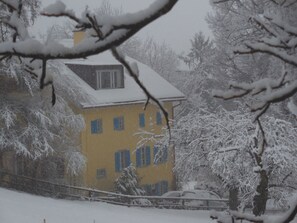 A yellow building with multiple windows and a snow-covered roof, surrounded by trees and a fence. - Haus Noains, (Rodels), by Interhome (Sils im Domleschg)