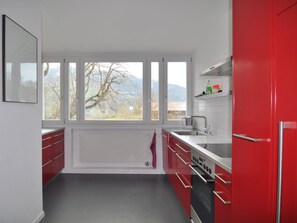 A kitchen with red cabinets, a white countertop, a stainless steel sink, and a view of trees and mountains through large windows.
