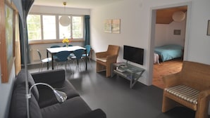 Een moderne woonkamer met een bank, een eettafel met stoelen, een televisie en een boekenkast.