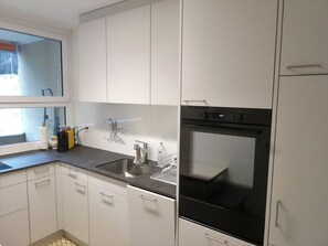 A modern kitchen with white cabinets, a stainless steel sink, and a black oven. - Viamalablick, (Thusis), by Interhome (Thusis)
