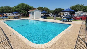 Una piscina rectangular con borde de azulejos, rodeada por una valla y con sombrillas.