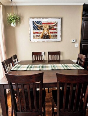 A dining room with a table, chairs, a framed picture of a bull with an American flag background, and a hanging plant. - Welcome to The Lone Star Stay! Relaxing 3/2 family/group retreat near downtown! (Kirby)