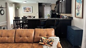 Una sala de estar con un sofá marrón, una cocina con barra y un comedor con sillas.