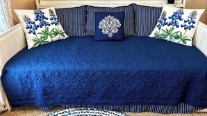 Una cama con colcha azul, almohadas a rayas y un cojín decorativo.