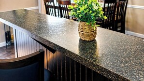 Una cocina con encimera de granito, una cesta de mimbre con plantas verdes y un comedor con sillas y mesa.
