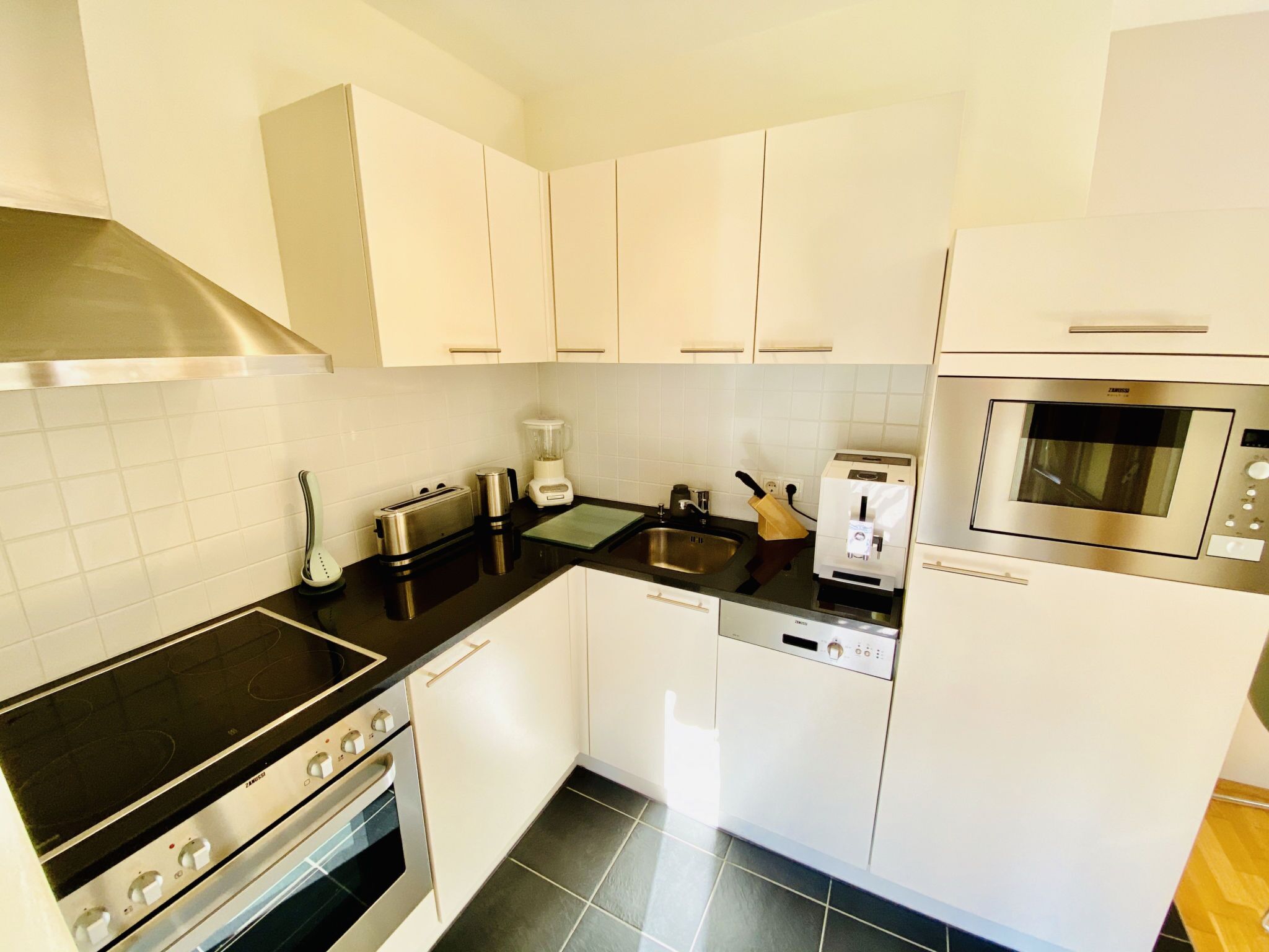 A kitchen with white cabinets, a stove, a microwave, a toaster, and a dishwasher.
