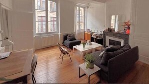 Een ruime woonkamer met een open haard, grote ramen en een eethoek.