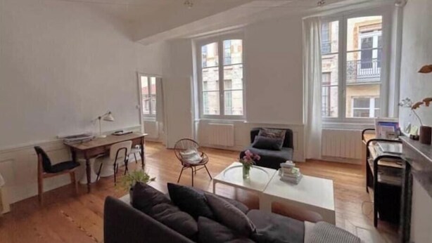 Een ruime woonkamer met een bank, salontafel en fauteuil. Grote ramen zorgen voor daglicht en uitzicht.
