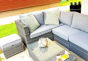 Un canapé modulable avec des coussins et un pouf assorti, une table basse en fibres tressées et un panier en osier.