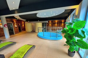 A modern indoor pool area with a glass railing, a large potted plant, and a wooden wall. - Apartment  by Interhome (Rauris)