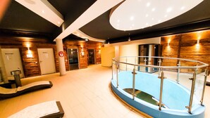 Un espace piscine intérieur moderne, doté d’une rambarde en verre, de murs en bois et d’une salle de massage.