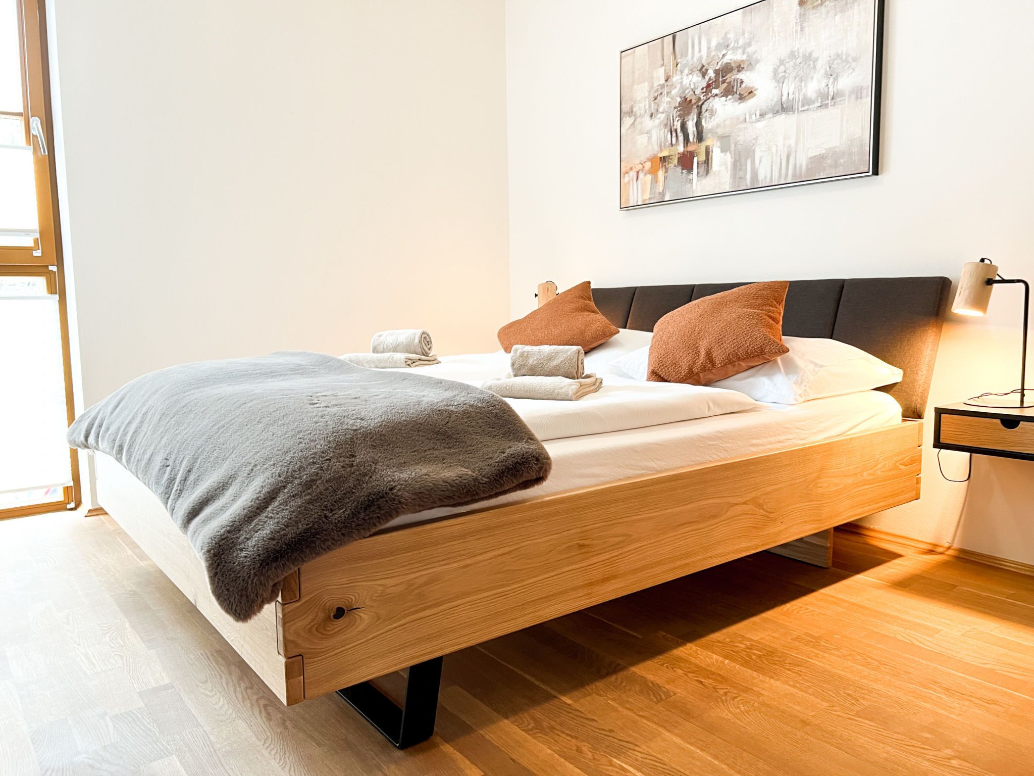 Une chambre à coucher moderne avec un lit en bois, une couverture grise et deux oreillers marron.