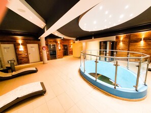 Ein moderner Poolbereich im Innenbereich mit Glasgeländer, Holzvertäfelung und einem Massageroom.