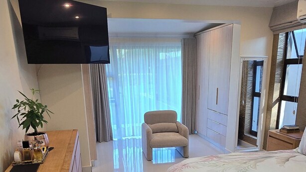 A modern hotel room with a large bed, a wooden dresser, a flat-screen TV, and a ceiling fan. - Fantastic 4-bedroom house in pleasant Gillitts for your getaway (Gillitts)