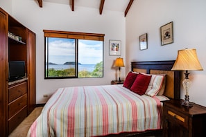 A bedroom with a bed, a TV, a window with a view, and two lamps.