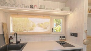Eine moderne Küche mit integriertem Spülbecken, einem Fenster mit Jalousien und einem Regal mit Geschirr und Gläsern.