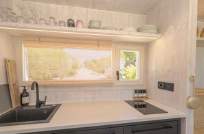 A modern kitchen with a built-in sink, a window with blinds, and a shelf with dishes and glasses. - Buqez - Villa 27 by Interhome (Pakoštane/Drage)